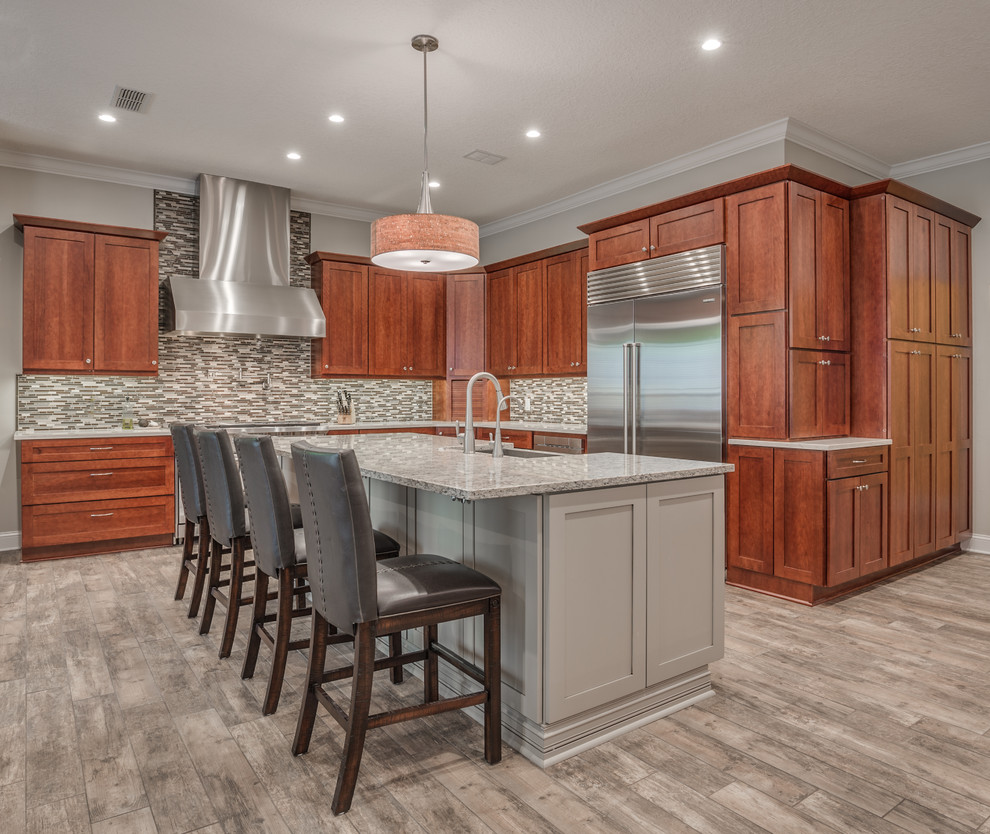Photo of a large traditional kitchen/diner in Jacksonville with a belfast sink, shaker cabinets, medium wood cabinets, engineered stone countertops, multi-coloured splashback, mosaic tiled splashback, stainless steel appliances, porcelain flooring and multiple islands.
