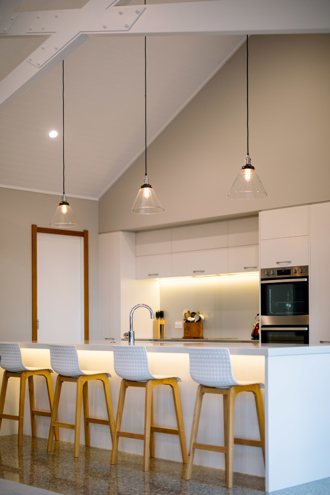 ハミルトンにあるカントリー風のおしゃれなキッチン (フラットパネル扉のキャビネット、白いキャビネット、グレーのキッチンパネル、ガラス板のキッチンパネル、コンクリートの床、グレーの床、白いキッチンカウンター) の写真