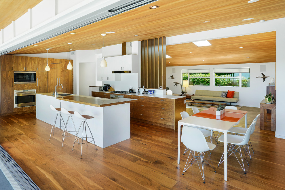 Design ideas for a midcentury l-shaped open plan kitchen in Los Angeles with a submerged sink, flat-panel cabinets, dark wood cabinets, stainless steel appliances, dark hardwood flooring, an island, brown floors and white worktops.