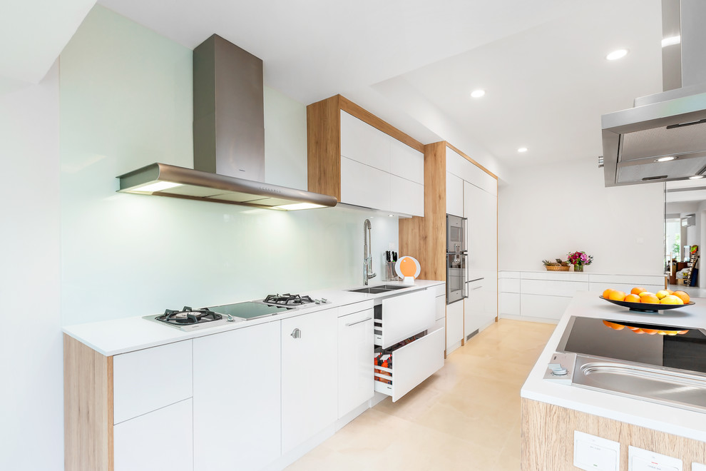 Bild på ett stort minimalistiskt kök, med en undermonterad diskho, släta luckor, vita skåp, vitt stänkskydd, stänkskydd i glaskakel, rostfria vitvaror och en köksö