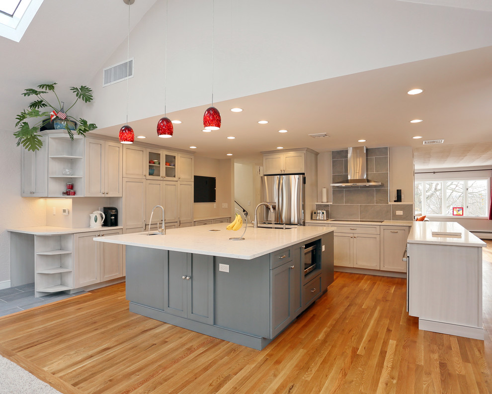 Design ideas for a large modern u-shaped kitchen/diner in Boston with a submerged sink, shaker cabinets, grey cabinets, engineered stone countertops, grey splashback, porcelain splashback, stainless steel appliances, light hardwood flooring and multiple islands.