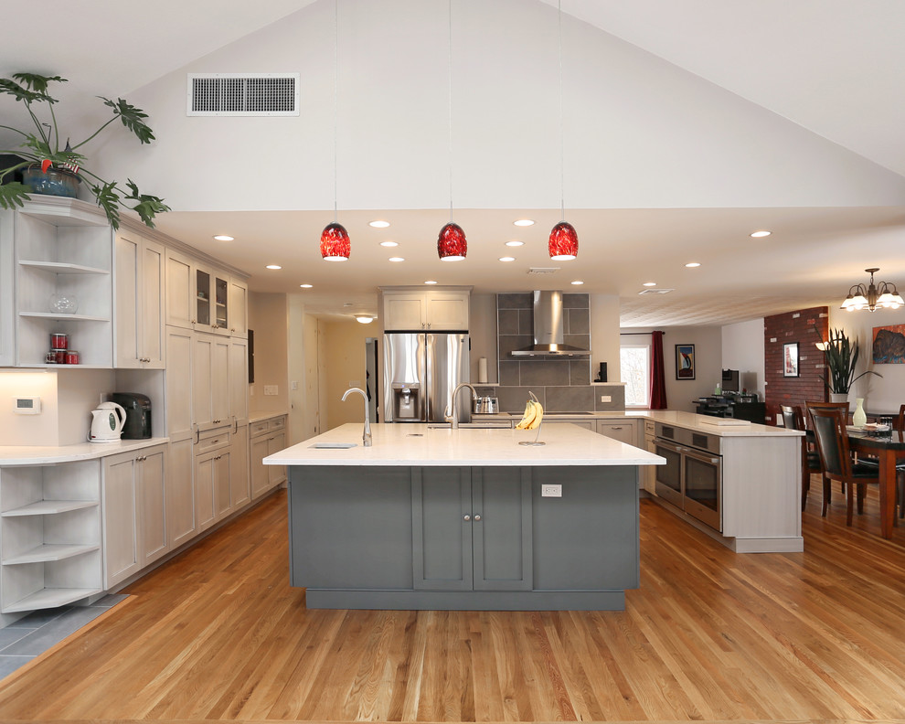 This is an example of a large classic u-shaped kitchen/diner in Boston with a submerged sink, shaker cabinets, grey cabinets, engineered stone countertops, grey splashback, porcelain splashback, stainless steel appliances, multiple islands and light hardwood flooring.