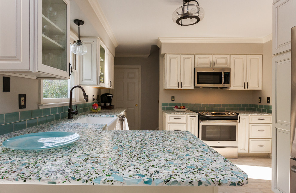 チャールストンにあるお手頃価格の中くらいなコンテンポラリースタイルのおしゃれなキッチン (エプロンフロントシンク、ガラス扉のキャビネット、白いキャビネット、再生ガラスカウンター、青いキッチンパネル、セラミックタイルのキッチンパネル、シルバーの調理設備、セラミックタイルの床、ベージュの床) の写真