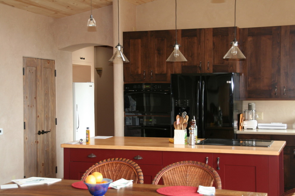 アルバカーキにある高級な中くらいなサンタフェスタイルのおしゃれなキッチン (ダブルシンク、レイズドパネル扉のキャビネット、クオーツストーンカウンター、ベージュキッチンパネル、黒い調理設備、ライムストーンの床) の写真