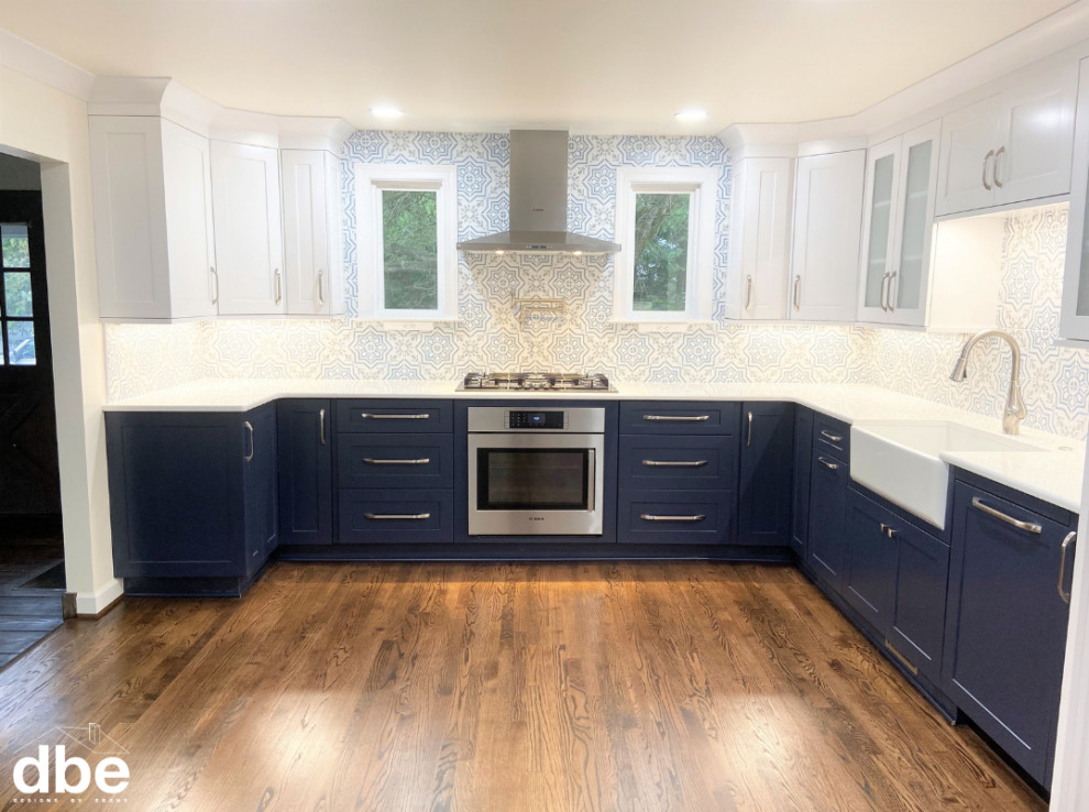 This is an example of a large traditional l-shaped kitchen/diner in Other with a belfast sink, shaker cabinets, blue cabinets, engineered stone countertops, multi-coloured splashback, porcelain splashback, stainless steel appliances, dark hardwood flooring, no island, brown floors and white worktops.
