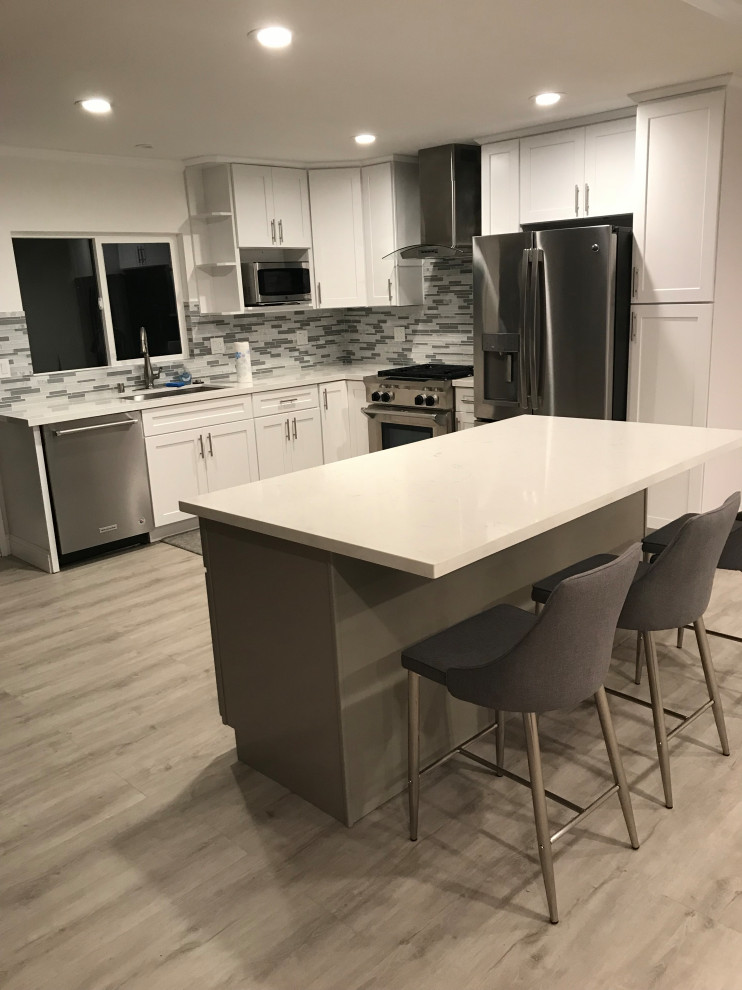 Immagine di una grande cucina minimal con lavello sottopiano, ante con riquadro incassato, ante bianche, top in quarzo composito, paraspruzzi multicolore, paraspruzzi con piastrelle a listelli, elettrodomestici in acciaio inossidabile, pavimento in laminato, pavimento grigio e top bianco