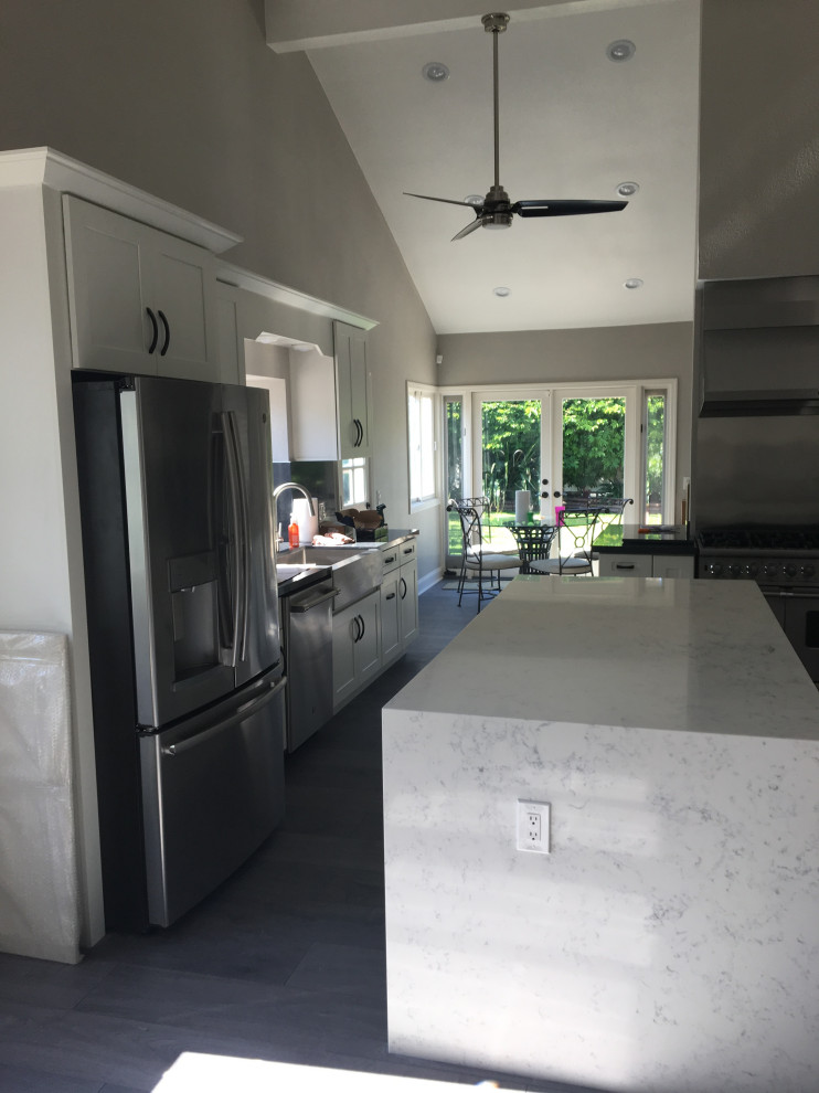 Idéer för att renovera ett mellanstort funkis vit vitt kök, med en rustik diskho, luckor med infälld panel, vita skåp, bänkskiva i kvarts, vitt stänkskydd, stänkskydd i keramik, rostfria vitvaror, vinylgolv, en köksö och grått golv