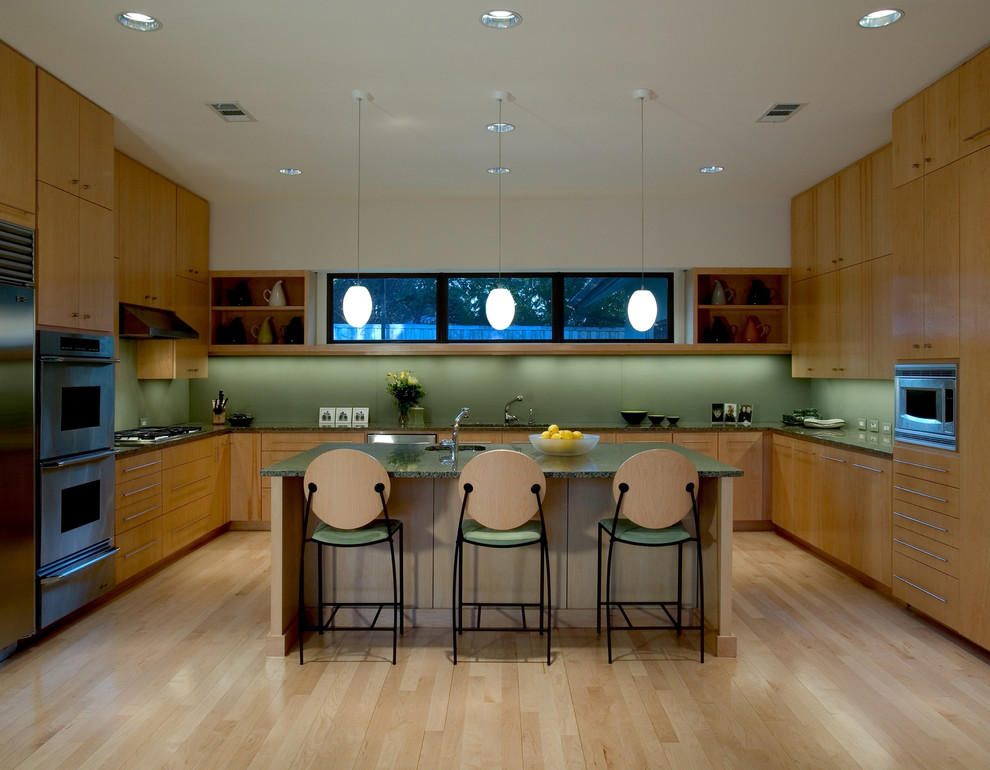 На фото: п-образная кухня в стиле ретро с монолитной мойкой, плоскими фасадами, фасадами цвета дерева среднего тона, зеленым фартуком и техникой из нержавеющей стали