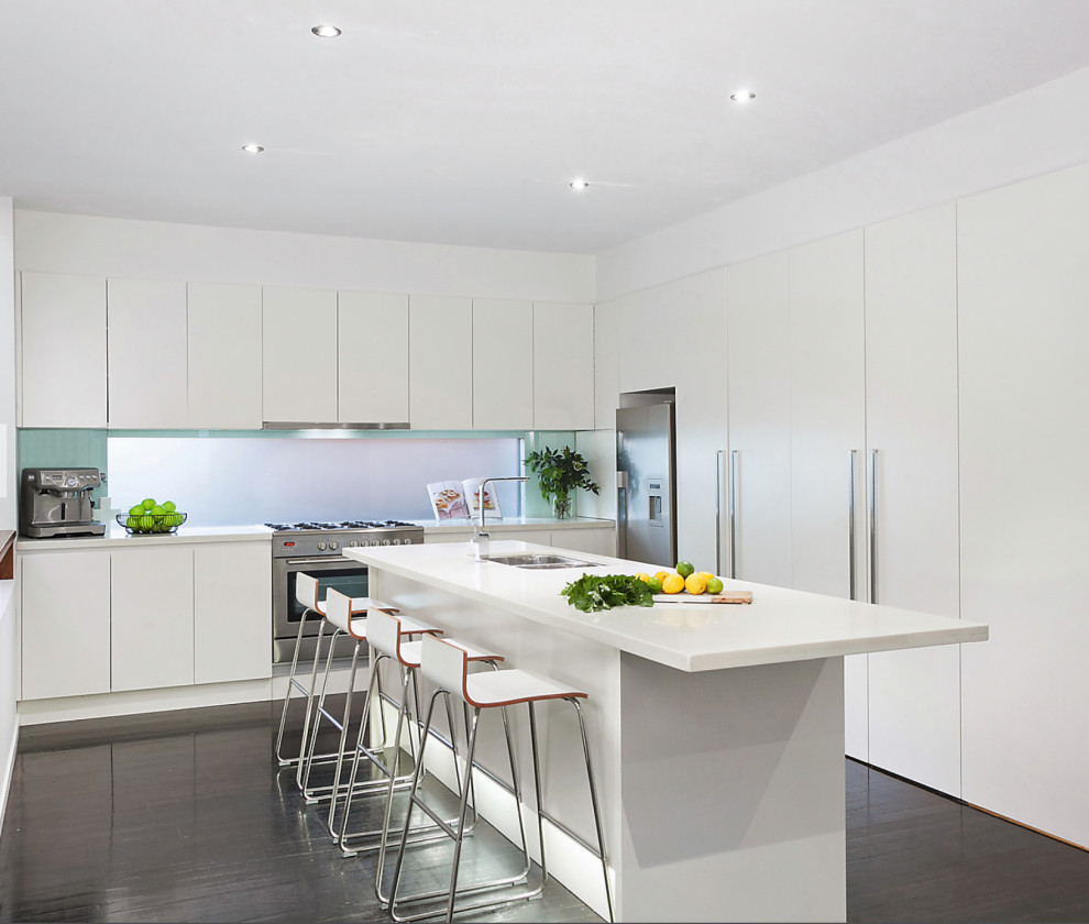Moderne Küche in U-Form mit flächenbündigen Schrankfronten, weißen Schränken, Küchengeräten aus Edelstahl, dunklem Holzboden, Kücheninsel, braunem Boden und weißer Arbeitsplatte in Sydney