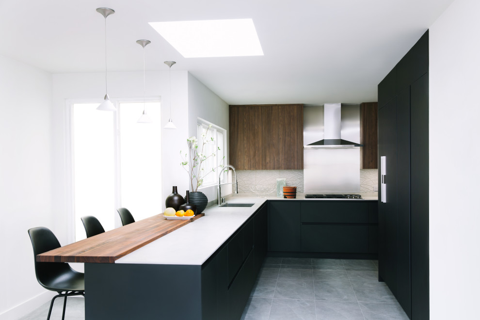 Foto på ett mellanstort funkis grå kök, med en undermonterad diskho, släta luckor, svarta skåp, grått stänkskydd, stänkskydd i stenkakel, rostfria vitvaror, klinkergolv i porslin, en halv köksö och grått golv