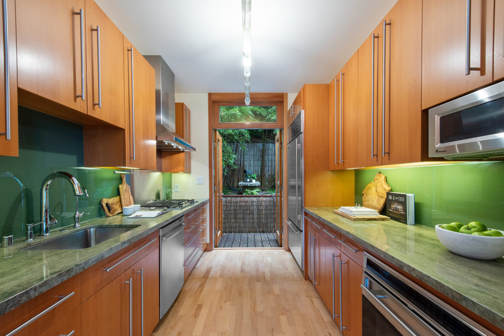 Small world-inspired galley enclosed kitchen in San Francisco with a single-bowl sink, flat-panel cabinets, light wood cabinets, marble worktops, green splashback, glass sheet splashback, stainless steel appliances, light hardwood flooring, no island, beige floors and green worktops.