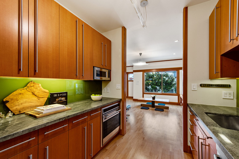 サンフランシスコにある高級な小さなアジアンスタイルのおしゃれなキッチン (アンダーカウンターシンク、フラットパネル扉のキャビネット、中間色木目調キャビネット、大理石カウンター、緑のキッチンパネル、ガラス板のキッチンパネル、シルバーの調理設備、淡色無垢フローリング、アイランドなし、茶色い床、緑のキッチンカウンター) の写真