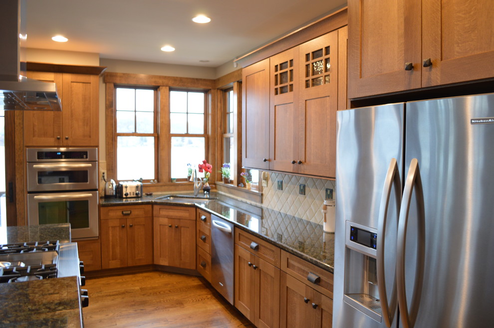 Mid-sized mountain style l-shaped medium tone wood floor open concept kitchen photo in New York with an undermount sink, shaker cabinets, medium tone wood cabinets, granite countertops, beige backsplash, ceramic backsplash, stainless steel appliances and an island