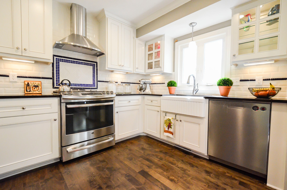 Example of a large classic l-shaped dark wood floor eat-in kitchen design in Kansas City with a farmhouse sink, shaker cabinets, white cabinets, quartz countertops, white backsplash, subway tile backsplash, stainless steel appliances and an island
