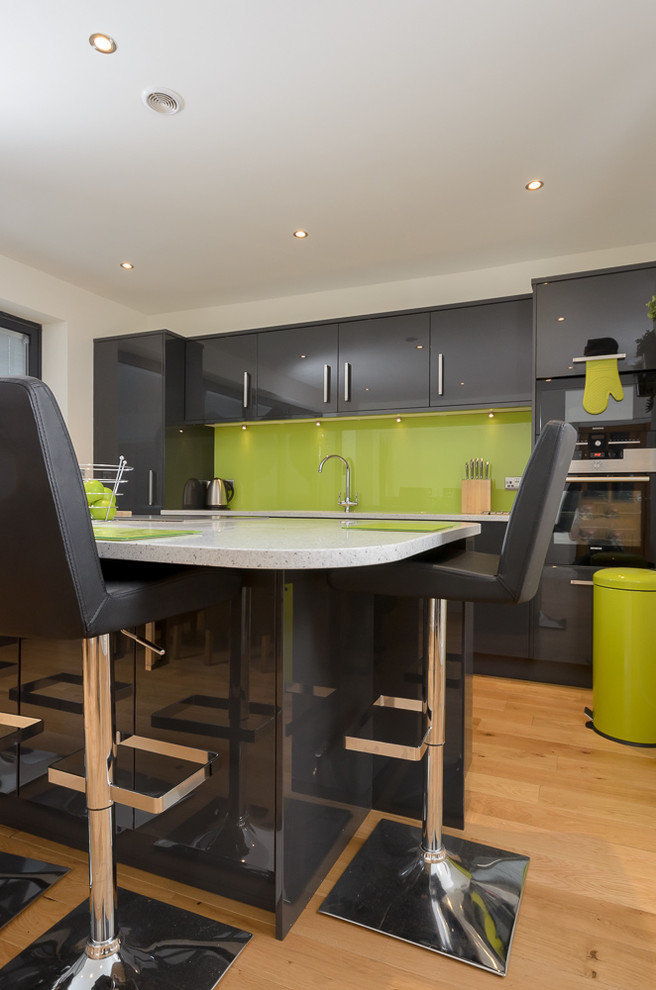 This is an example of a modern single-wall kitchen/diner in Other with a built-in sink, flat-panel cabinets, grey cabinets, composite countertops, green splashback, glass sheet splashback, integrated appliances, vinyl flooring and an island.