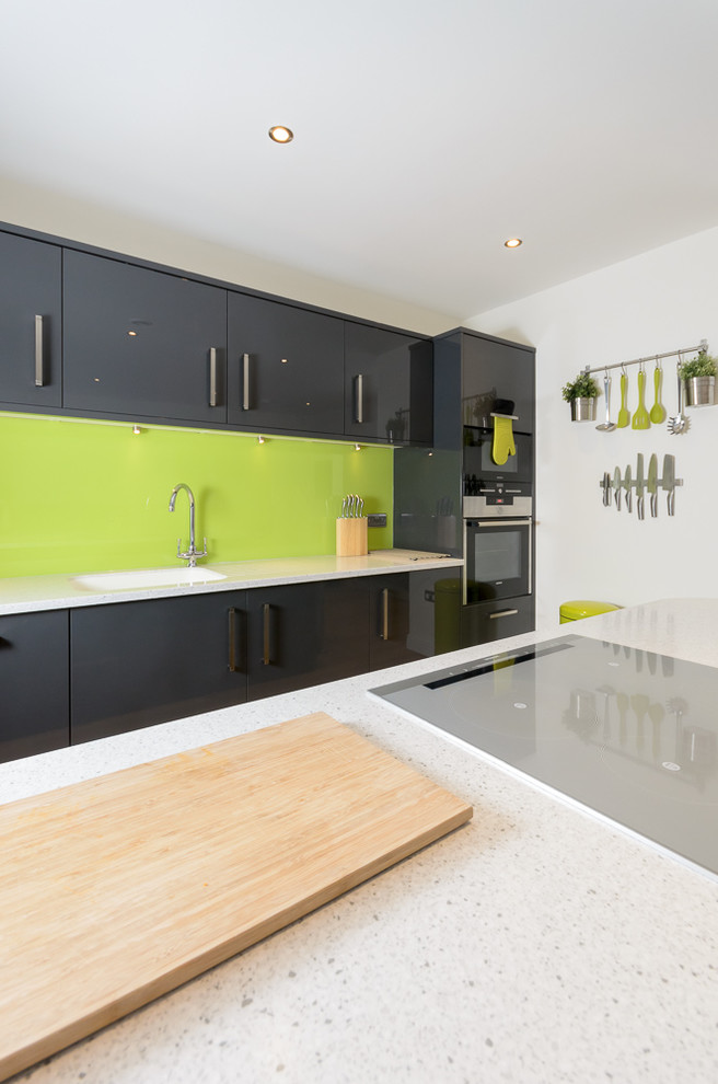 Design ideas for a modern single-wall kitchen/diner in Other with a built-in sink, flat-panel cabinets, grey cabinets, composite countertops, green splashback, glass sheet splashback, integrated appliances, vinyl flooring and an island.