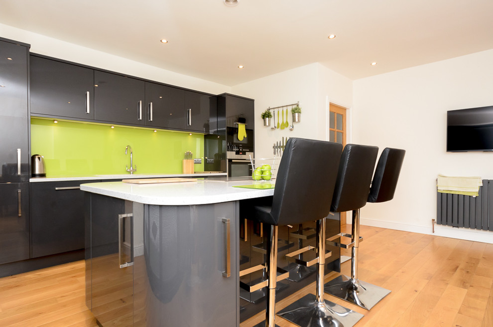 Modern single-wall kitchen/diner in Other with a built-in sink, flat-panel cabinets, grey cabinets, composite countertops, green splashback, glass sheet splashback, integrated appliances, vinyl flooring and an island.