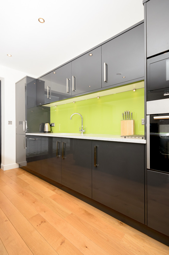 Immagine di una cucina moderna con lavello da incasso, ante lisce, ante grigie, top in superficie solida, paraspruzzi verde, paraspruzzi con lastra di vetro, elettrodomestici da incasso e pavimento in vinile