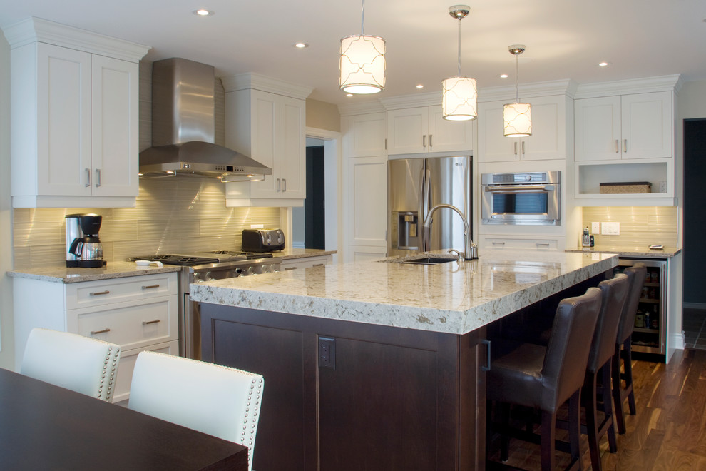 This is an example of a traditional kitchen in Ottawa with a double-bowl sink, recessed-panel cabinets, white cabinets, engineered stone countertops, grey splashback, glass tiled splashback, stainless steel appliances, medium hardwood flooring and an island.