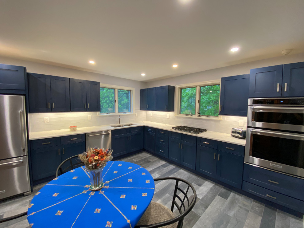This is an example of a medium sized classic l-shaped kitchen in New York with a submerged sink, shaker cabinets, blue cabinets, engineered stone countertops, white splashback, glass tiled splashback, stainless steel appliances, porcelain flooring, no island, multi-coloured floors and white worktops.