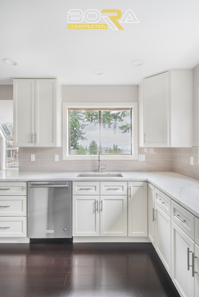 Design ideas for a large classic l-shaped open plan kitchen in Seattle with a submerged sink, shaker cabinets, white cabinets, engineered stone countertops, beige splashback, ceramic splashback, stainless steel appliances, dark hardwood flooring, an island, brown floors and white worktops.