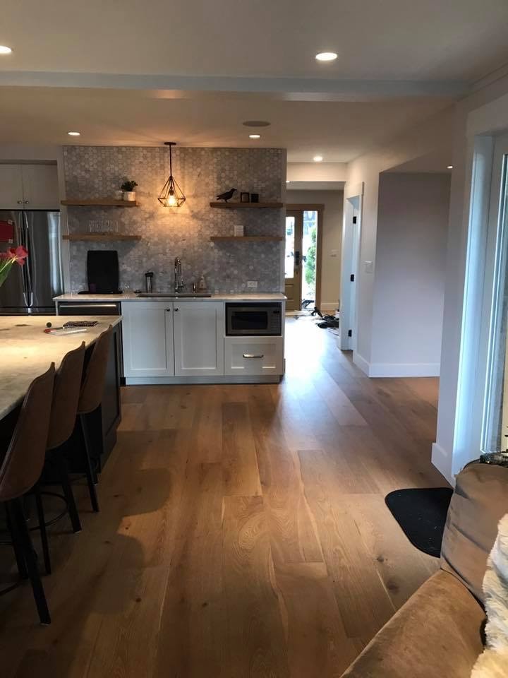 Photo of a medium sized traditional u-shaped kitchen/diner in Vancouver with a submerged sink, shaker cabinets, white cabinets, marble worktops, grey splashback, stainless steel appliances, medium hardwood flooring, an island, glass sheet splashback and brown floors.