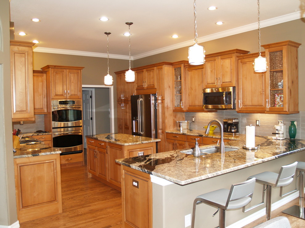 Example of a mid-sized classic u-shaped medium tone wood floor and brown floor eat-in kitchen design in Denver with a double-bowl sink, raised-panel cabinets, medium tone wood cabinets, quartz countertops, beige backsplash, glass tile backsplash, stainless steel appliances and an island