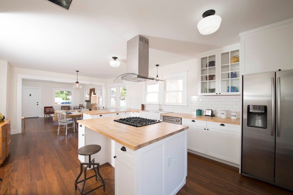 Mid-sized arts and crafts l-shaped dark wood floor eat-in kitchen photo in Los Angeles with a farmhouse sink, shaker cabinets, white cabinets, wood countertops, white backsplash, subway tile backsplash, stainless steel appliances and an island