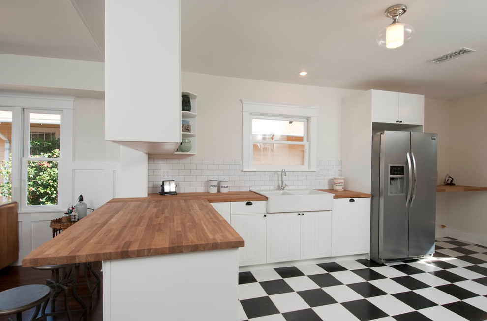 Amerikansk inredning av ett mellanstort kök, med en halv köksö, luckor med profilerade fronter, vita skåp, träbänkskiva, vitt stänkskydd, stänkskydd i tunnelbanekakel, rostfria vitvaror, en rustik diskho och klinkergolv i keramik