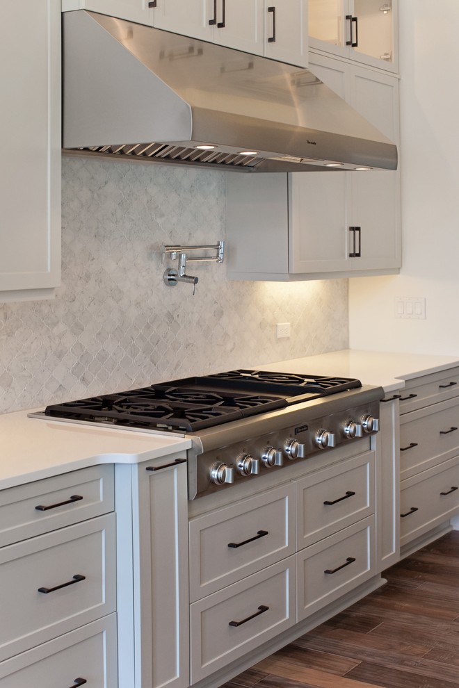 Example of a huge transitional medium tone wood floor open concept kitchen design in Jacksonville with a farmhouse sink, recessed-panel cabinets, white cabinets, quartz countertops, gray backsplash, mosaic tile backsplash, stainless steel appliances and an island