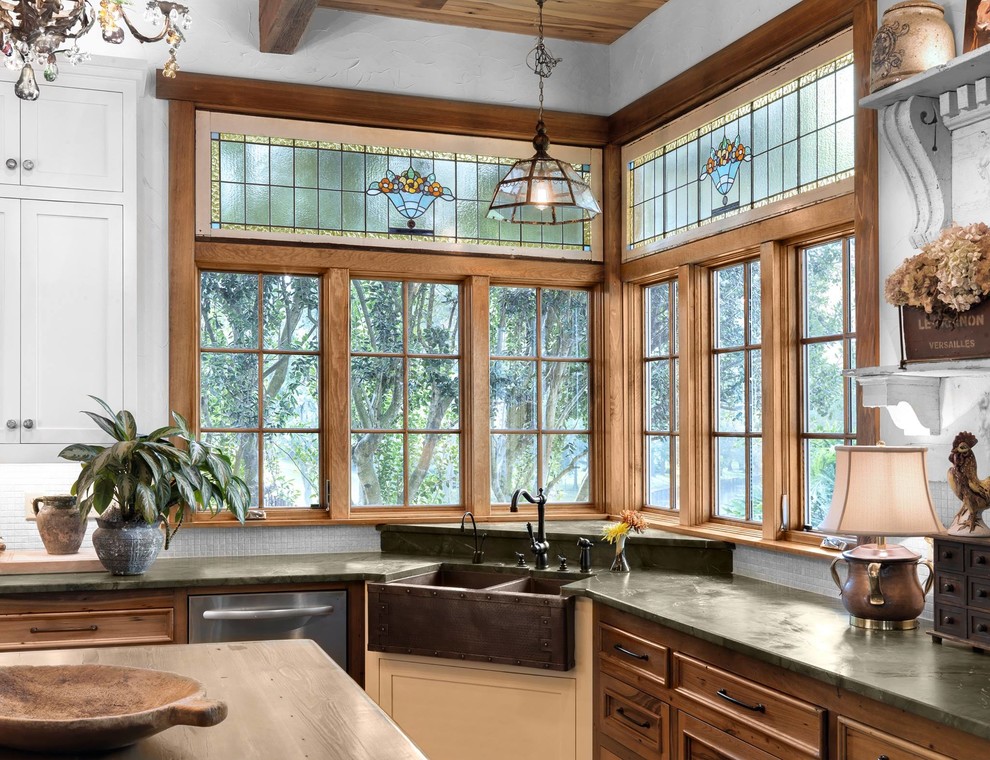 Example of a classic l-shaped kitchen design in Other with a farmhouse sink, recessed-panel cabinets, medium tone wood cabinets, white backsplash, mosaic tile backsplash, stainless steel appliances, an island and black countertops
