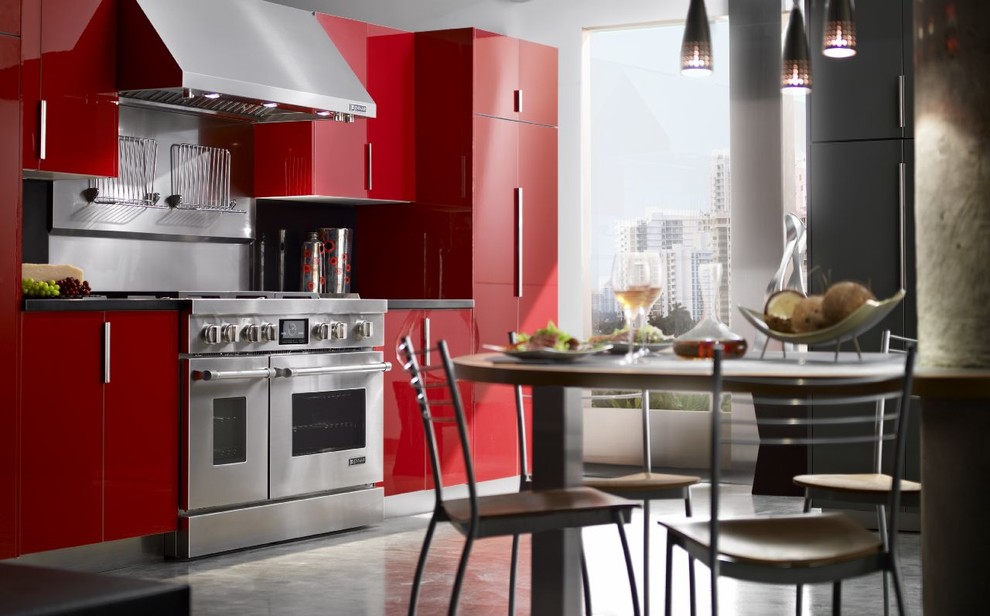 Пример оригинального дизайна: кухня в современном стиле с обеденным столом, красными фасадами и техникой из нержавеющей стали