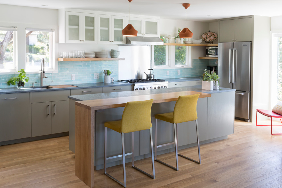 Modern inredning av ett mellanstort grå grått kök, med släta luckor, rostfria vitvaror, en köksö, grå skåp, ljust trägolv, brunt golv, en undermonterad diskho, bänkskiva i täljsten, blått stänkskydd och stänkskydd i stickkakel