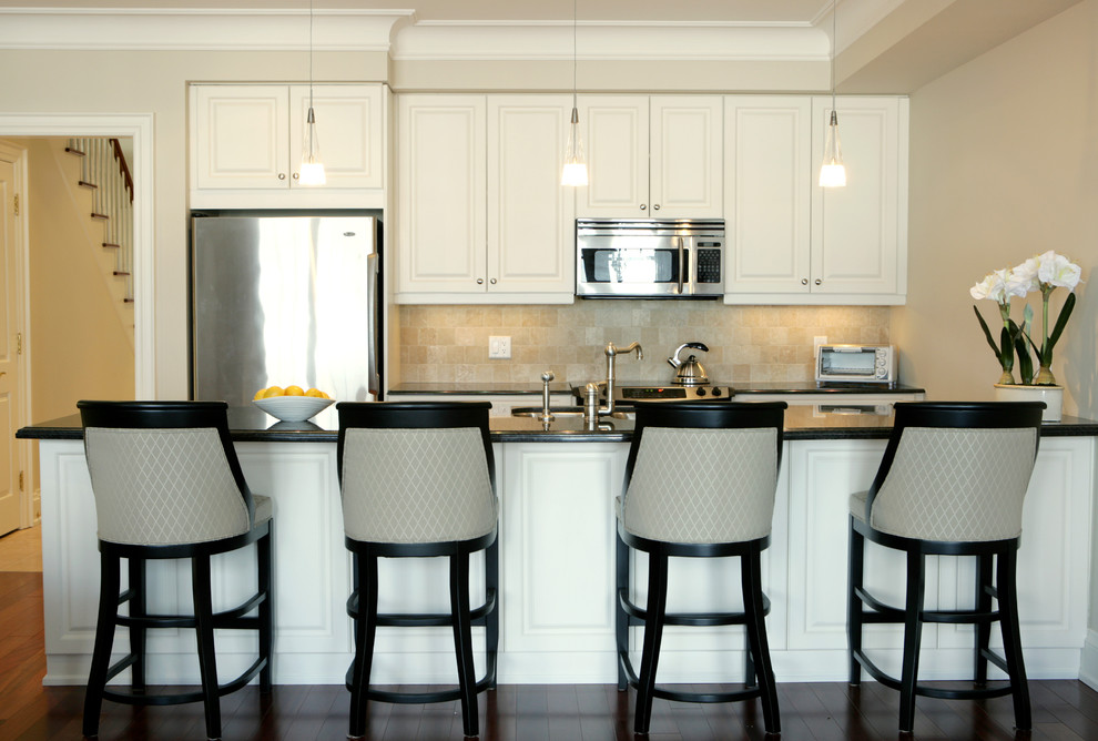 Exempel på ett mellanstort klassiskt kök, med en undermonterad diskho, luckor med upphöjd panel, vita skåp, beige stänkskydd, rostfria vitvaror, mörkt trägolv, granitbänkskiva, stänkskydd i stenkakel och en köksö