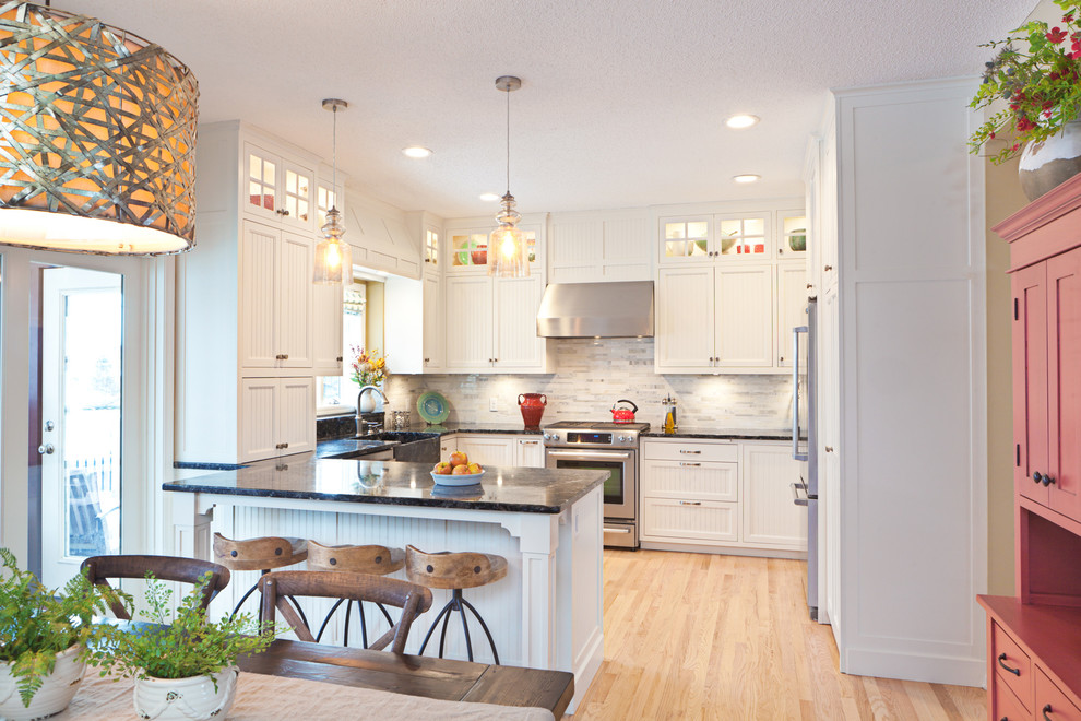 Bild på ett mellanstort lantligt kök, med en rustik diskho, vita skåp, granitbänkskiva, vitt stänkskydd, stänkskydd i stenkakel, rostfria vitvaror, ljust trägolv, en halv köksö och luckor med profilerade fronter