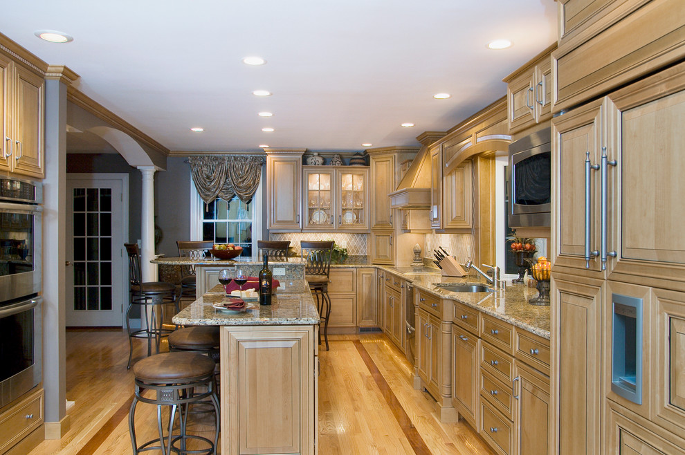 Klassische Küche mit zwei Kücheninseln, profilierten Schrankfronten, hellbraunen Holzschränken, Granit-Arbeitsplatte, Küchenrückwand in Beige, Rückwand aus Keramikfliesen und Elektrogeräten mit Frontblende in Boston