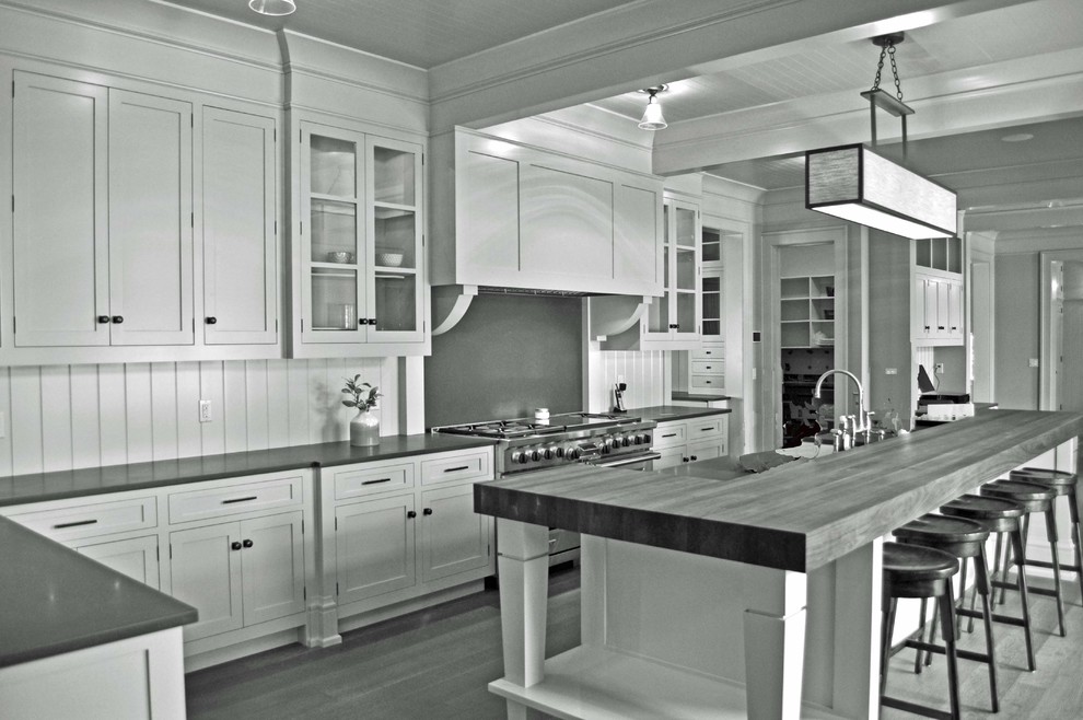 Inredning av ett modernt stort kök, med skåp i shakerstil, vita skåp, träbänkskiva, vitt stänkskydd, rostfria vitvaror, mellanmörkt trägolv och en köksö