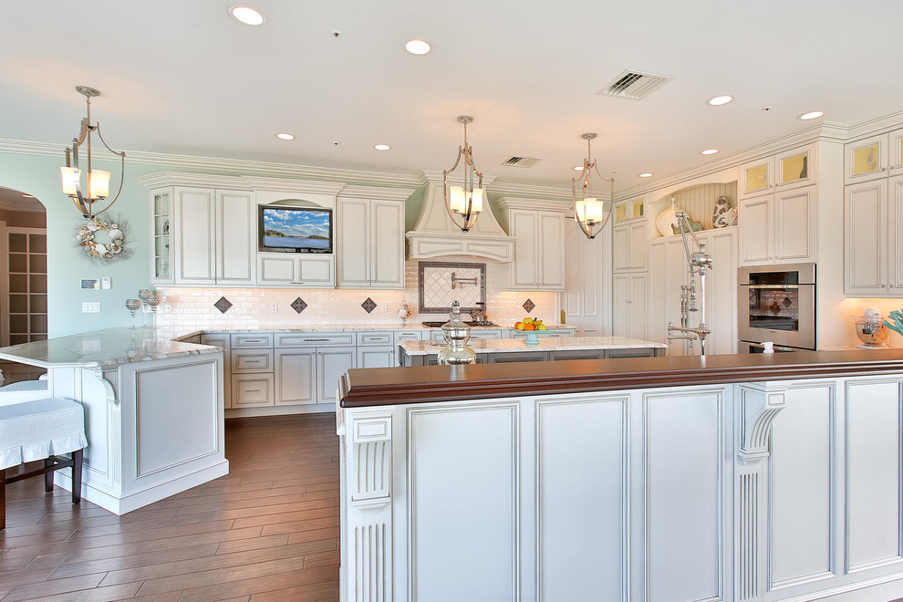 Example of a large transitional l-shaped dark wood floor eat-in kitchen design in New York with a farmhouse sink, recessed-panel cabinets, white cabinets, wood countertops, white backsplash, ceramic backsplash, paneled appliances and an island