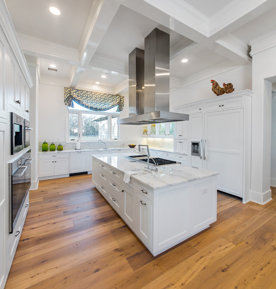 Klassische Küche in U-Form mit Schrankfronten im Shaker-Stil, weißen Schränken, Küchenrückwand in Weiß, Elektrogeräten mit Frontblende, braunem Holzboden und Kücheninsel in Dallas