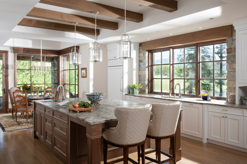 Example of a classic medium tone wood floor and exposed beam kitchen design in Other with an undermount sink, raised-panel cabinets, granite countertops, gray backsplash, stone tile backsplash, stainless steel appliances, an island and blue countertops