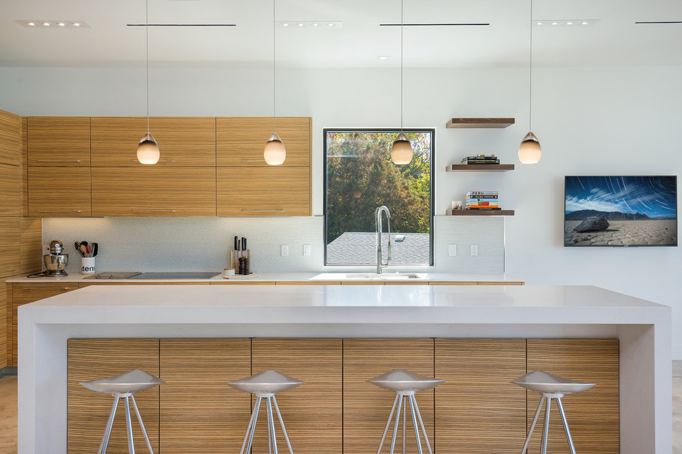 На фото: кухня в современном стиле с врезной мойкой, плоскими фасадами, светлыми деревянными фасадами, серым фартуком и островом с