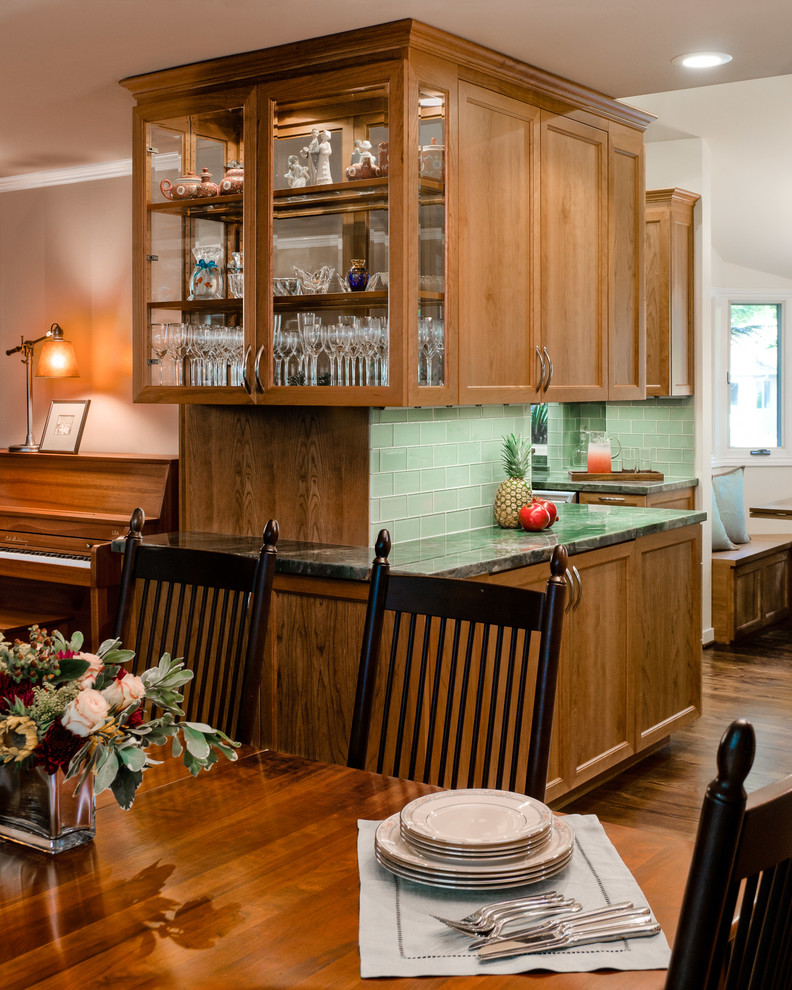 Inredning av ett klassiskt mellanstort kök, med en undermonterad diskho, luckor med infälld panel, skåp i mellenmörkt trä, bänkskiva i kvartsit, grönt stänkskydd, stänkskydd i glaskakel, rostfria vitvaror och mellanmörkt trägolv