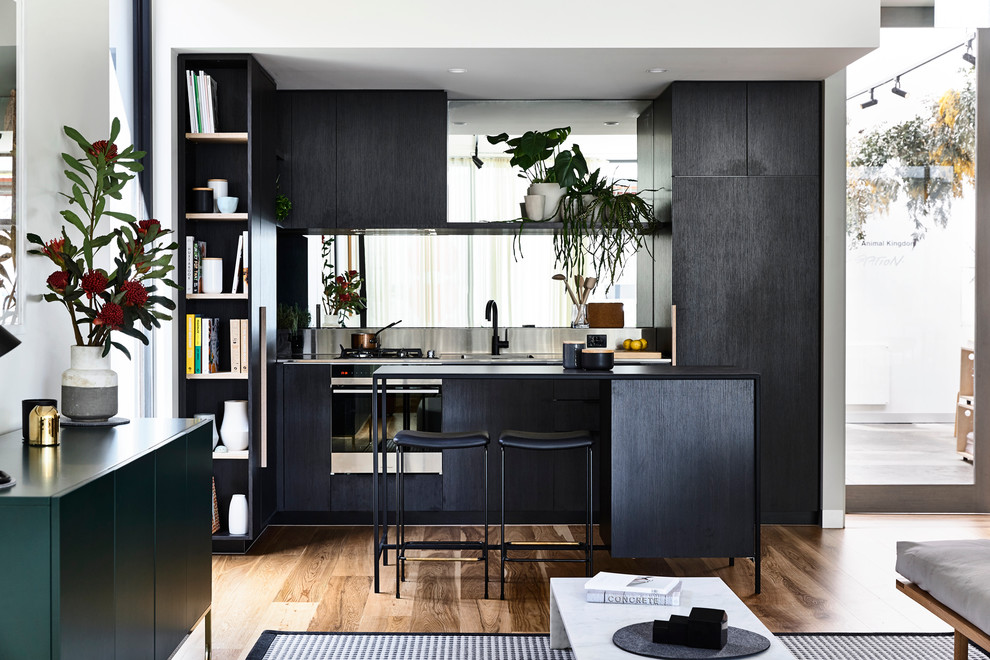 Bild på ett litet minimalistiskt kök, med en integrerad diskho, svarta skåp, bänkskiva i rostfritt stål, spegel som stänkskydd, rostfria vitvaror och en köksö
