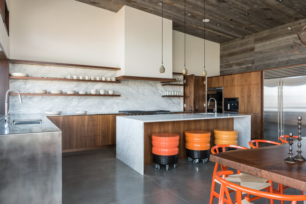 This is an example of a large rustic l-shaped kitchen/diner in Other with an island, a submerged sink, flat-panel cabinets, medium wood cabinets, marble worktops, white splashback, stainless steel appliances and concrete flooring.