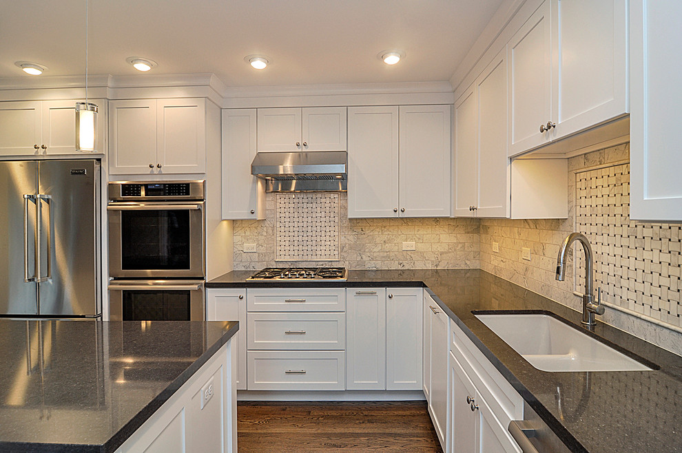 Foto på ett mellanstort amerikanskt kök, med en dubbel diskho, skåp i shakerstil, vita skåp, bänkskiva i kvarts, vitt stänkskydd, stänkskydd i mosaik, rostfria vitvaror, mörkt trägolv och en köksö