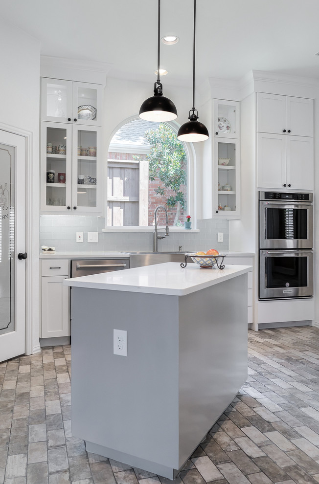 Bild på ett mellanstort lantligt vit vitt kök, med en rustik diskho, skåp i shakerstil, vita skåp, bänkskiva i kvarts, blått stänkskydd, stänkskydd i glaskakel, rostfria vitvaror, klinkergolv i porslin, en köksö och grått golv