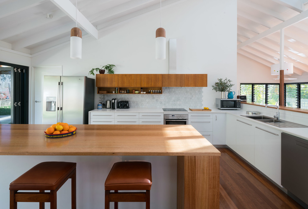 Moderne Küche in L-Form mit Doppelwaschbecken, flächenbündigen Schrankfronten, weißen Schränken, Küchenrückwand in Weiß, Rückwand aus Mosaikfliesen, Küchengeräten aus Edelstahl, Kücheninsel und braunem Holzboden in Brisbane