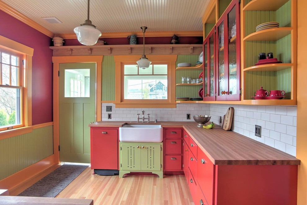 Foto på ett lantligt l-kök, med en rustik diskho, luckor med glaspanel, röda skåp, träbänkskiva, vitt stänkskydd, stänkskydd i tunnelbanekakel och ljust trägolv