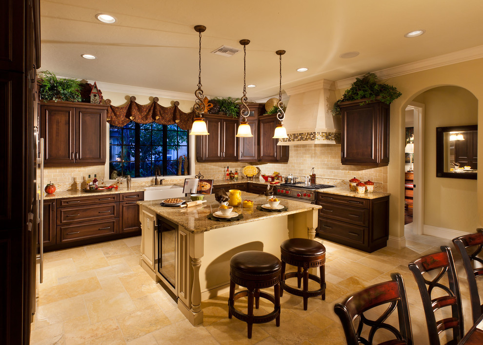 Inspiration for a large mediterranean u-shaped limestone floor open concept kitchen remodel in Tampa with a farmhouse sink, raised-panel cabinets, dark wood cabinets, granite countertops, beige backsplash, stone tile backsplash, stainless steel appliances and an island