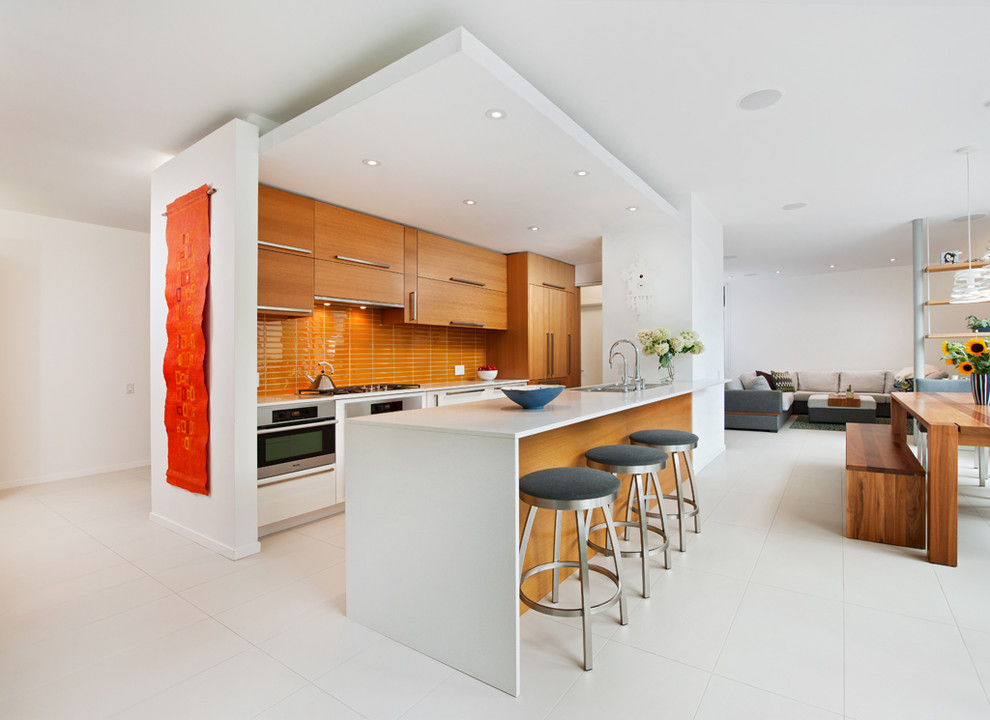 Стильный дизайн: параллельная кухня-гостиная в современном стиле с плоскими фасадами, фасадами цвета дерева среднего тона, оранжевым фартуком, техникой из нержавеющей стали и полуостровом - последний тренд
